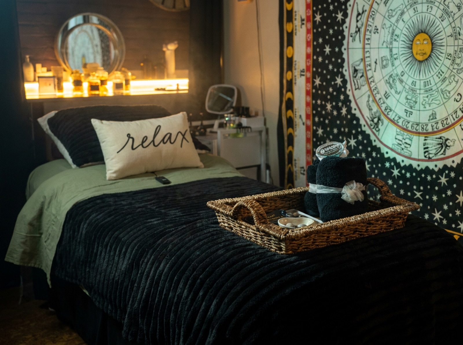Treatment bed dressed in sage and charcoal beside the zodiac tapestry